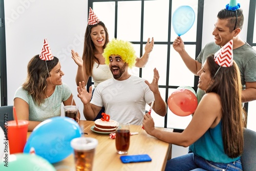 Group of young hispanic friends smiling happy surprise man with birthday cake at home.