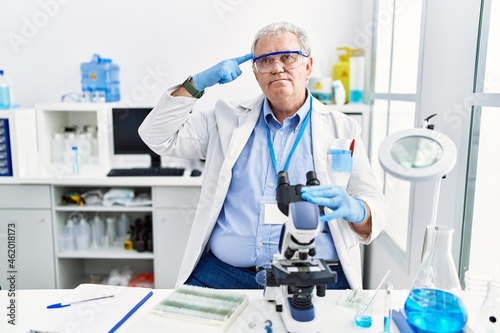 Senior caucasian man working at scientist laboratory smiling pointing to head with one finger  great idea or thought  good memory