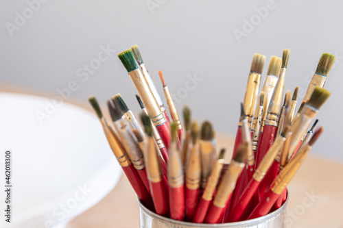 Close-up of red paint brushes in a metal jar.