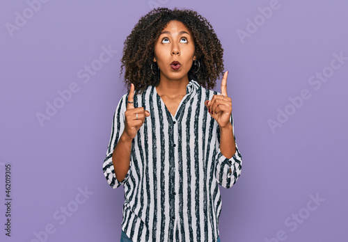 Young african american girl wearing casual clothes amazed and surprised looking up and pointing with fingers and raised arms. © Krakenimages.com