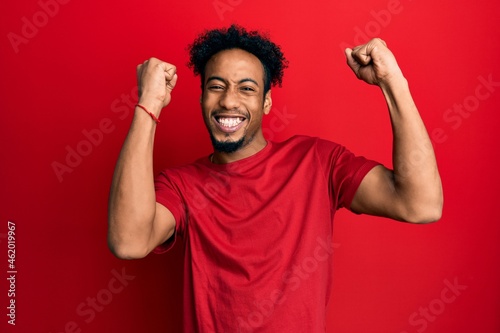 Young african american man with beard wearing casual red t shirt celebrating surprised and amazed for success with arms raised and open eyes. winner concept.