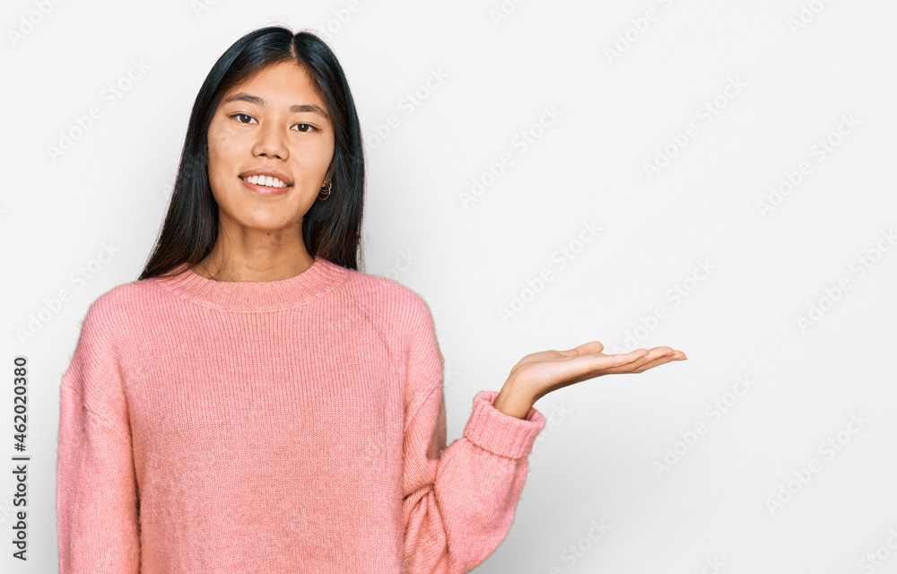 Beautiful young asian woman wearing casual winter sweater smiling cheerful presenting and pointing with palm of hand looking at the camera. Beautiful young asian woman wearing casual winter sweater smiling cheerful presenting and pointing with palm of hand looking at the camera.