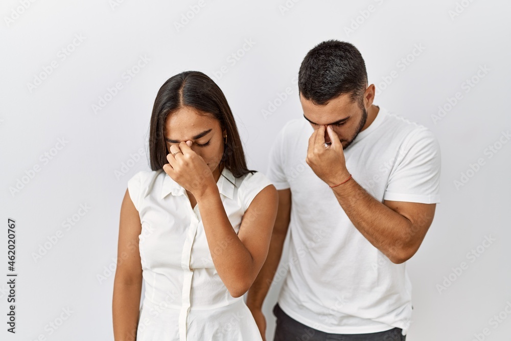 Young interracial couple standing together in love over isolated background tired rubbing nose and eyes feeling fatigue and headache. stress and frustration concept. Young interracial couple standing together in love over isolated background tired rubbing nose and eyes feeling fatigue and headache. stress and frustration concept.