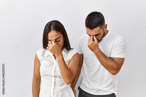 Young interracial couple standing together in love over isolated background tired rubbing nose and eyes feeling fatigue and headache. stress and frustration concept.