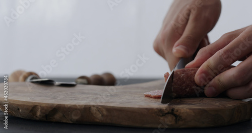 man slicing salami on olive board