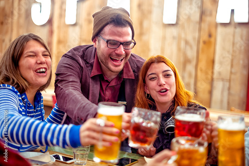 Group of happy friends clinking draft beer mugs in pub - Smiling boy and girls with beer in their hands toasting at the restaurant in the happy hour time - Friendship and youth concept