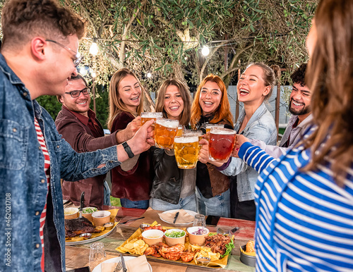 Sticker Happy boys and girls toasting beer in the garden of restaurant - Group of friends sitting on a summer terrace with beer in their hands and bbq on the table - Friendship and youth concept