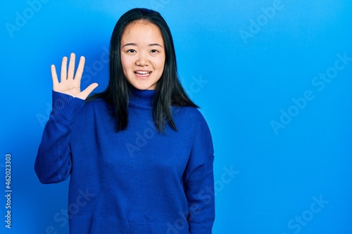 Young chinese girl wearing casual clothes showing and pointing up with fingers number five while smiling confident and happy.