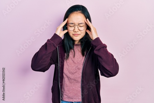 Young chinese girl wearing casual clothes and glasses suffering from headache desperate and stressed because pain and migraine. hands on head. © Krakenimages.com