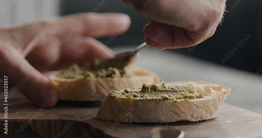 spread pesto on fresh baguette slice to make sandwich closeup spread pesto on fresh baguette slice to make sandwich closeup