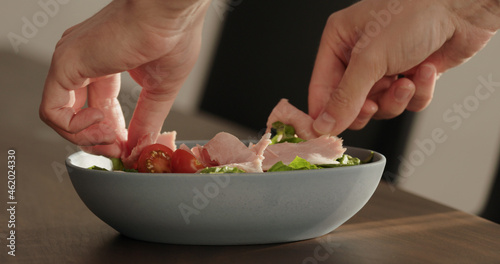 add prosciutto cotto on greens in blue bowl on walnut table making salad