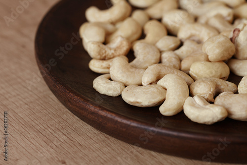 Tasty cashew nuts on a wooden plate on a wooden table, side view. Space for text