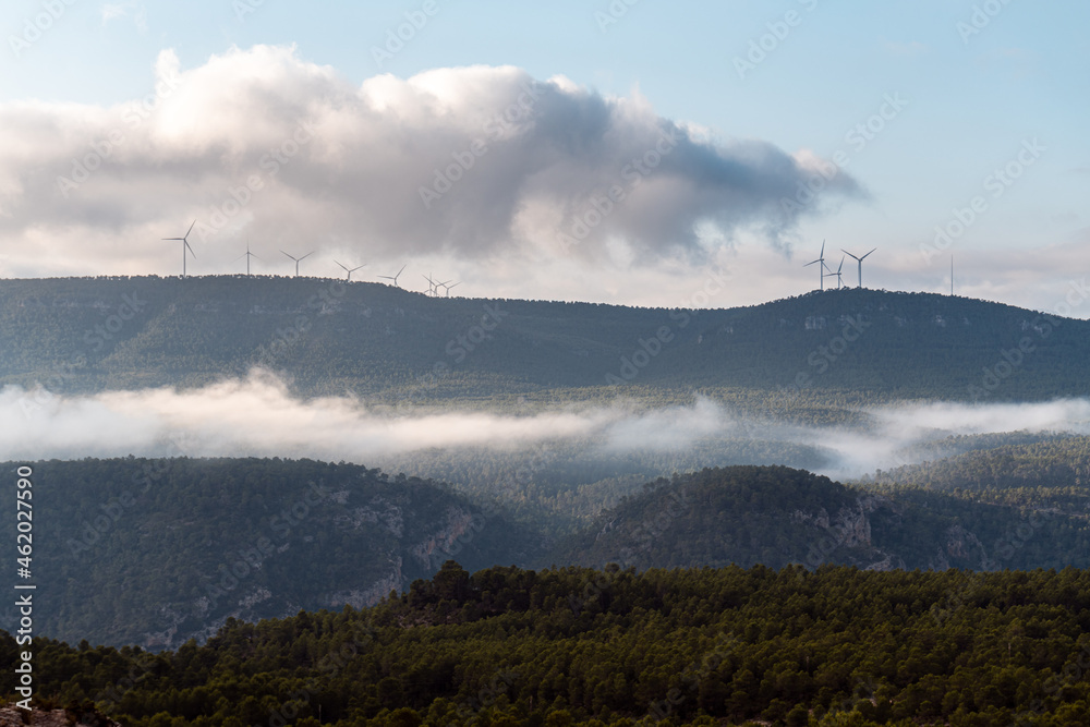 Mountainous landscape, with large pine forests partially covered in mist, on a cool autumn morning. 