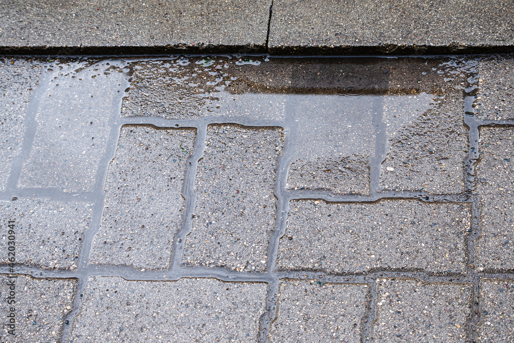 A puddle after rain on an uneven tile surface. Improperly laid gray paving slabs. Errors in