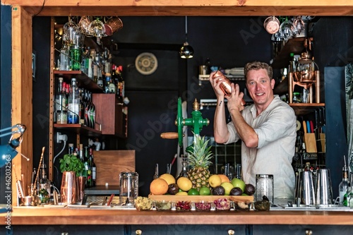 View of a cheerful man working as bartender in a colourful cocktail bar, view of a professional barman shaking a drink behind the counter, Lisbon, Portugal.