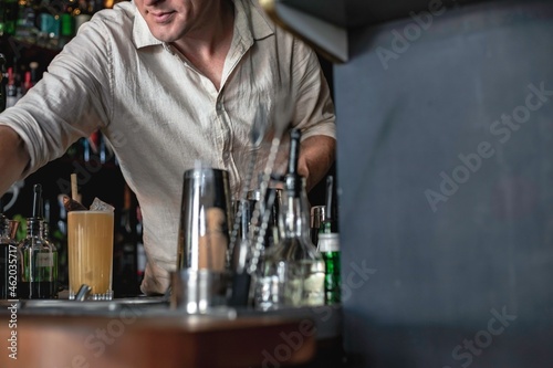 A professional bartender working in a fancy cocktail bar serving a colourful tropical drink while standing behind the counter in a night club.