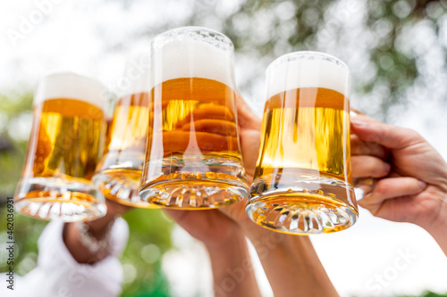 Group of people enjoying and toasting a beer outdoors - Close-up on four pint of beer photo