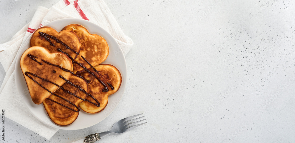 Pancakes in shape of breakfast hearts with chocolate sauce in gray ceramic plate, cup of coffee on gray concrete background. Table setting for Valentines Day breakfast. Top view copy space. Banner.