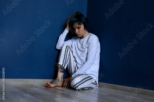 Young girl with head down is cornered among blue walls. Concept of mental illness.