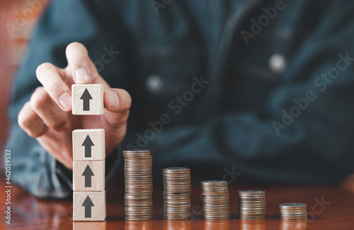 Businessman putting wooden cube box arrow with stack coins on desk. Saving money, bank deposits, interest collection and tax concept. Upward trend in business growth, financial management