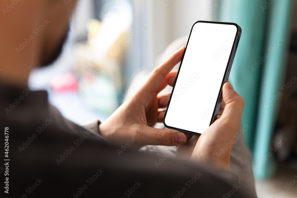 Man using smartphone blank screen frameless modern design while sitting on the chair in home interior - obrazy, fototapety, plakaty 