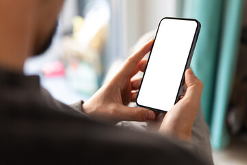 Man holding a modern smartphone with blank screen in a home interior. Ideal for app mockups, mobile UI/UX, tech communication or advertising. High-res image with copy space on screen