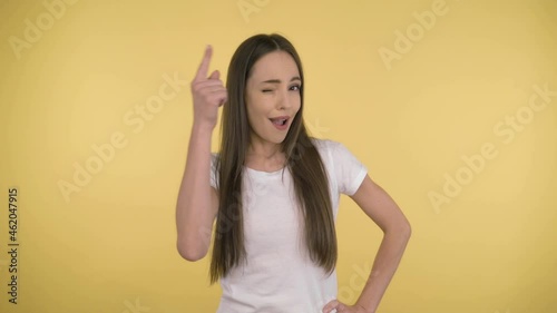 Portrait of a cute attractive woman 40 years old on an isolated yellow background in the studio. Long-haired woman in a basic white t-shirt reflects over the proposal