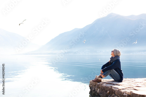 Young woman relaxing at winter sea beach. Traveler resting by blue mountain photo