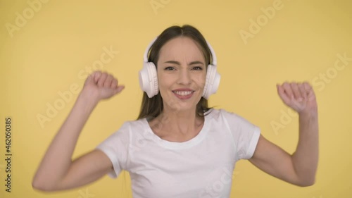 Funny attractive woman 35 years old middle age on yellow background in studio in profile. Woman fun dancing listening to music in large white wireless headphones