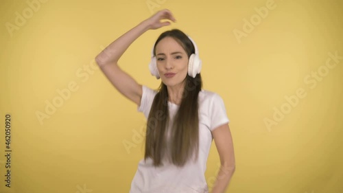 Funny attractive woman 35 years old middle age on yellow background in studio in profile. Woman fun dancing listening to music in large white wireless headphones
