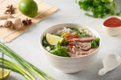 Pho Bo Soup with beef, rice noodles, ginger, lime, chili pepper in bowl on white backgound. Close up. Vietnamese and Asian cuisine. photo