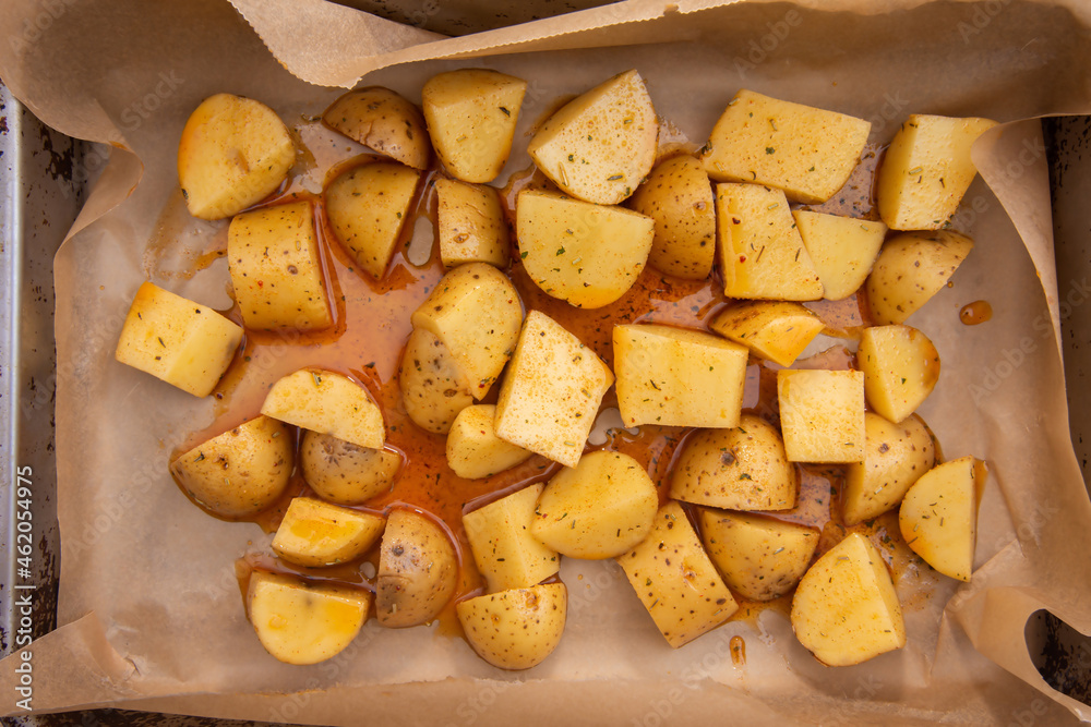 Chopped fresh potatoes into small pieces and drizzled with oil and spices to prepare American potatoes by baking in the oven Chopped fresh potatoes into small pieces and drizzled with oil and spices to prepare American potatoes by baking in the oven