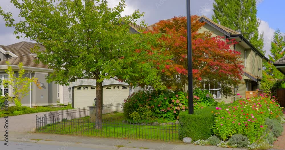 Establishing shot of two story stucco luxury house with garage door, big tree and nice landscape in Vancouver, Canada, North America. Day time on June 2021. ProRes 422 HQ.