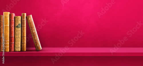 Row of old books on pink shelf. Background banner