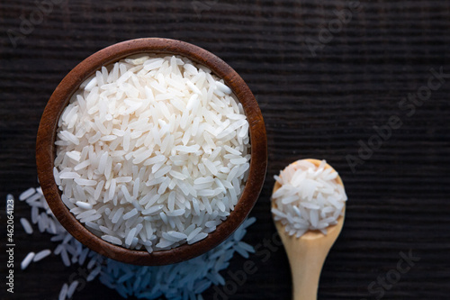 Top view of white rice in wooden bowl on  dark wooden table.