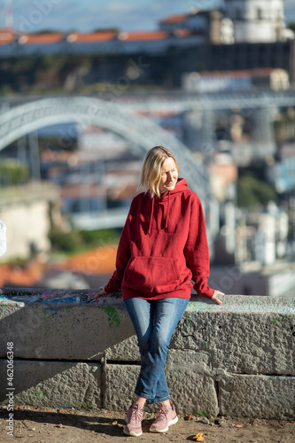 A woman in a hoodie in old town Porto, Portugal. Louis iron Bridge in the blur in the background.