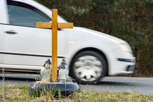 A roadside memorial cross with a candles commemorating the tragic death, on a background ride blurred car.