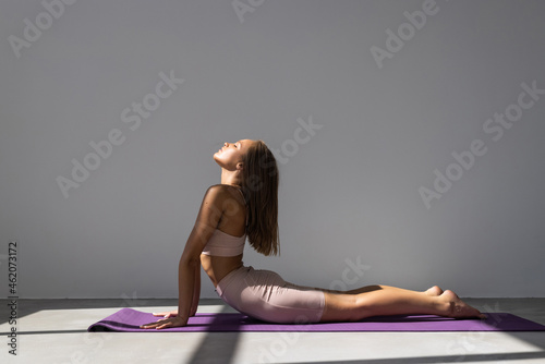Young attractive woman practicing yoga, stretching in Cobra exercise, Bhujangasana pose, working out wearing sportswear, indoor full length, isolated against white background
