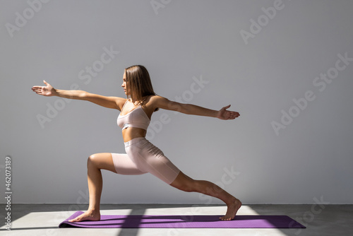 Portrait of sporty fit beautiful young brunette woman in sportswear working out, doing Utthita Trikonasana, Extended Triangle pose on white background
