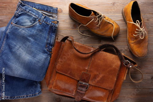 Denim jeans and old boots with leather bag at wood table. Travel concept as retro clothes