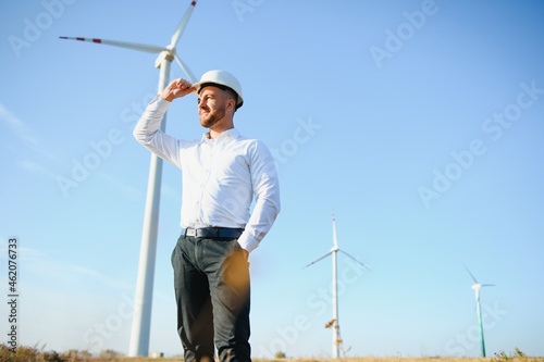 Engineer is checking energy production on wind turbine. Worker in windmills park in helmet.