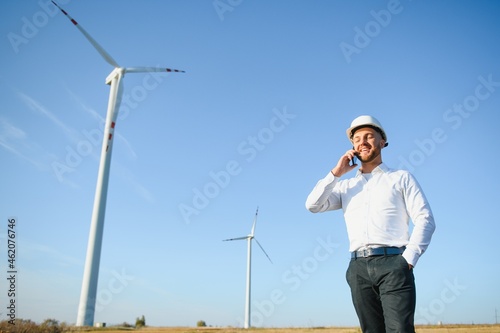 Young Businessman Talking to Manager Using Smart Telephone On Wind Turbine Field, Green Energy Concept