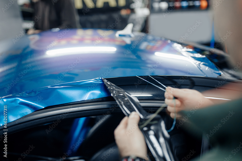 Obraz premium Car wrapping specialist putting vinyl foil or film on car. Selective focus.