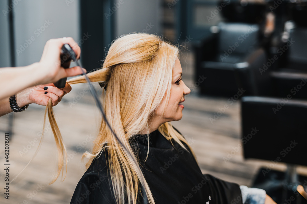 Beautiful blond middle-aged woman enjoying in modern hair salon.