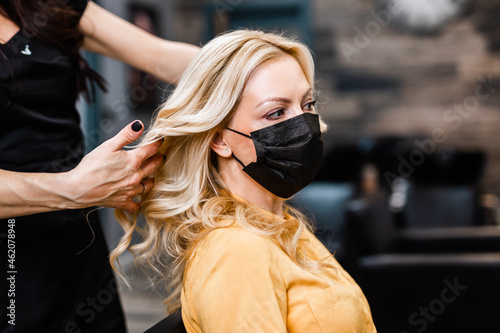 Beautiful hairstyle of middle-aged woman with protective face mask after dyeing hair in hair salon.