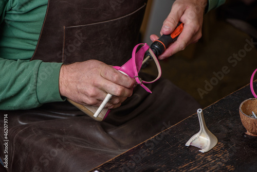 Obraz na płótnie Shoemaker in leather apron repairing broken heel on women's pink shoes in workshop. Shoe repair concept. w salonie