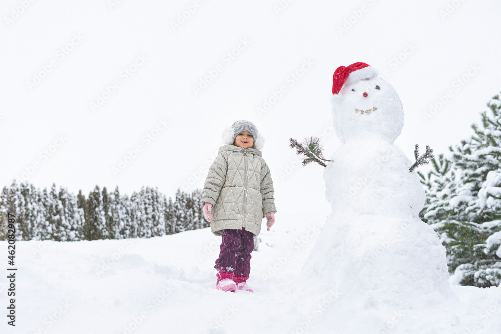 child builds a snowman in the winter in the yard. concept of winter games with snow for children