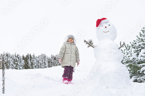 child builds a snowman in the winter in the yard. concept of winter games with snow for children