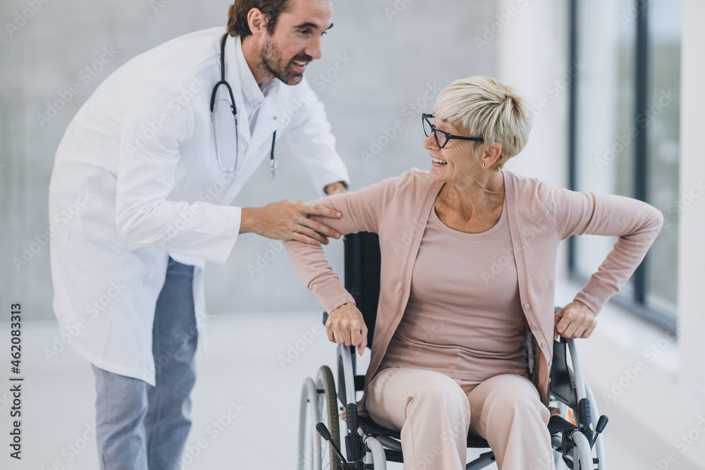Senior Woman Using A Wheelchair Along The Hospital Hallway And Talking With Her Doctor Senior Woman Using A Wheelchair Along The Hospital Hallway And Talking With Her Doctor