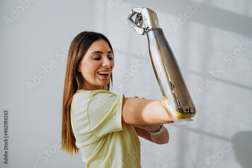 Portrait of a strong and independent woman with a bionic prosthetic arm shows a bicep on a light background looks at the camera and smiles photo